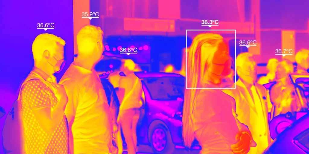 A thermal camera image of several people on a city street in oranges and purples